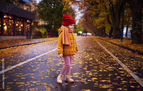 Stylish Little Girl Smiling on Colorful Autumn Street – Cozy Autumn Vibe in Warm Clothes and Colorful Fall Leaves