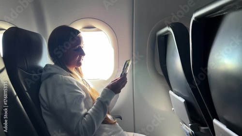 Happy woman glancing at her phone near airplane window.