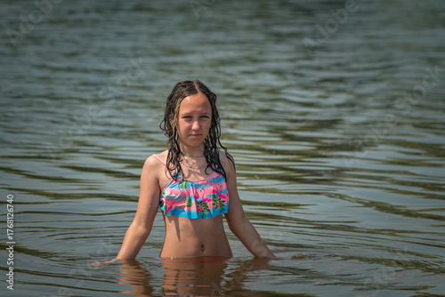 Young girl with long dark hair joyfully splashing water while playing in a lake, wearing a colorful swimsuit, capturing the essence of summer fun and carefree childhood moments