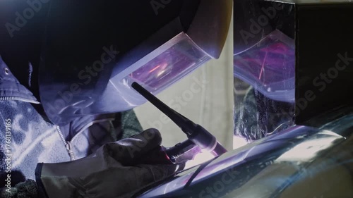 An industrious and technical mood is captured by a close-up of a welder in protective gear using a welding torch, with the bright arc and reflection visible in the shield and surrounding surfaces