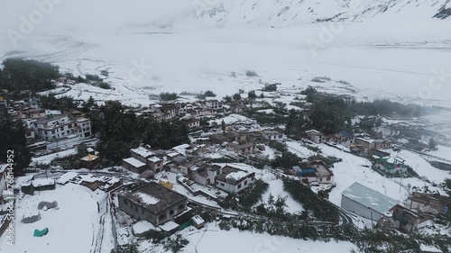 Aerial drone shot of traditional Ladakhi village houses and structures partially covered in snow in the Himalayan mountains.