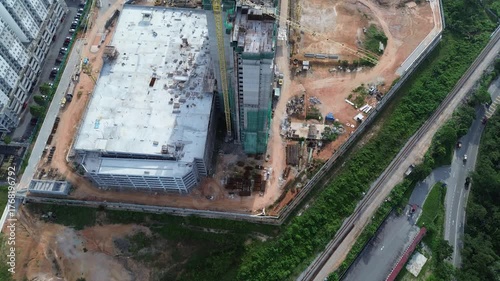 Aerial drone shot of a massive commercial construction site, showing a tall crane and development of a large building complex next to urban residential areas and a railway.