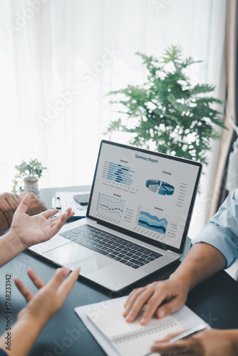 Business data analysis concept with colleagues reviewing financial report on laptop, pointing at chart with growth graph, teamwork discussing statistics, planning strategy and corporate success.
