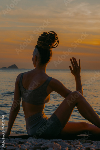 Skinny woman with dreadlocks doing yoga with sea as backdrop