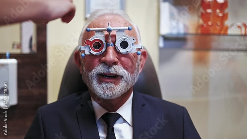 Professional optometrist examining a senior patient's vision with a phoropter trial frame during an appointment in the ophthalmology clinic, selecting the correct lenses for prescription glasses