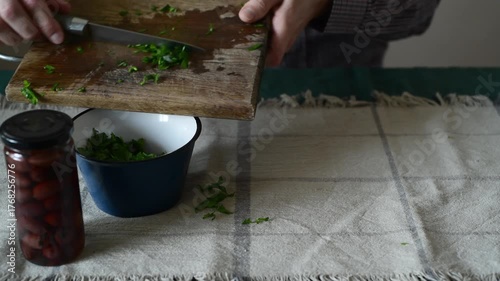 A man pours chopped parsley into a bowl.