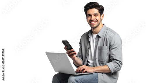 Smiling man in gray shirt uses laptop and holds phone, against a white background, isolated cutout