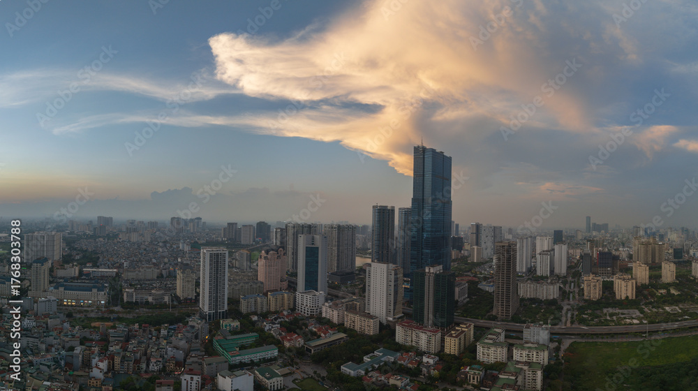 Fototapeta premium Evening panorama of Hanoi skyline with dramatic golden clouds behind a tall skyscraper.