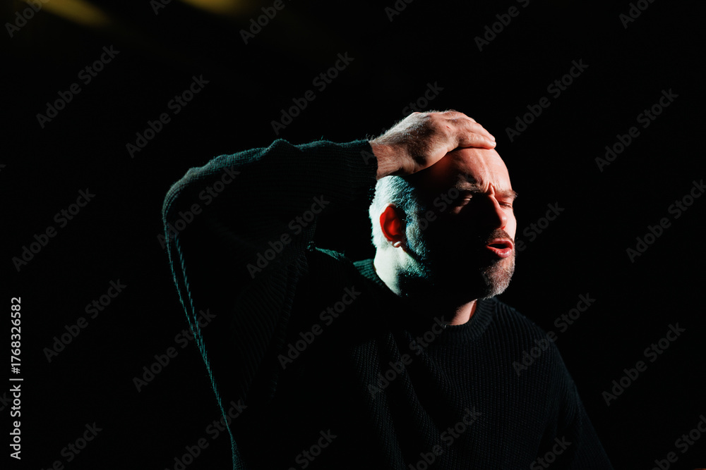 Fototapeta premium Emotional actor in sweatshirt rehearsing on stage with black background 