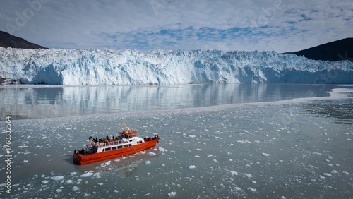 An awe inspiring aerial perspective captures a modern cruise ship gracefully navigating the icy waters in front of the colossal Eqi Glacier in Greenland