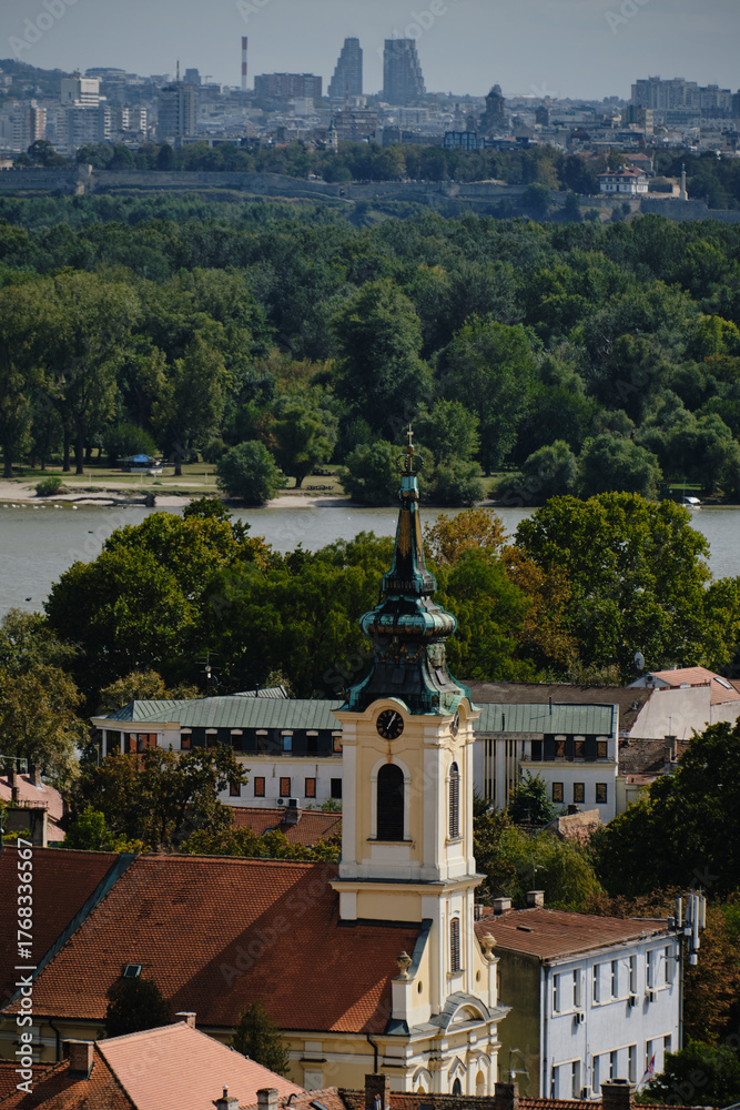 Fototapeta premium Zemun church tower with green roof and view of Belgrade skyline across the Danube River
