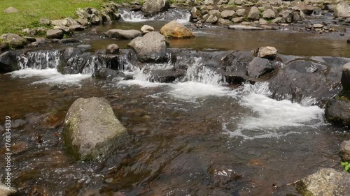 Crystal clear mountain stream with white water foam flowing over rocks and pebbles under daylight. Seamless 4K loop ideal for calm, meditation, or nature backgrounds