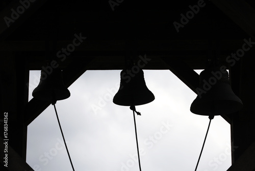 Church bells silhouettes in a bell tower against a bright sky