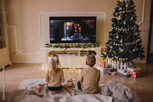 Bild auf Leinwand Children Watching Christmas Movie by Decorated Tree