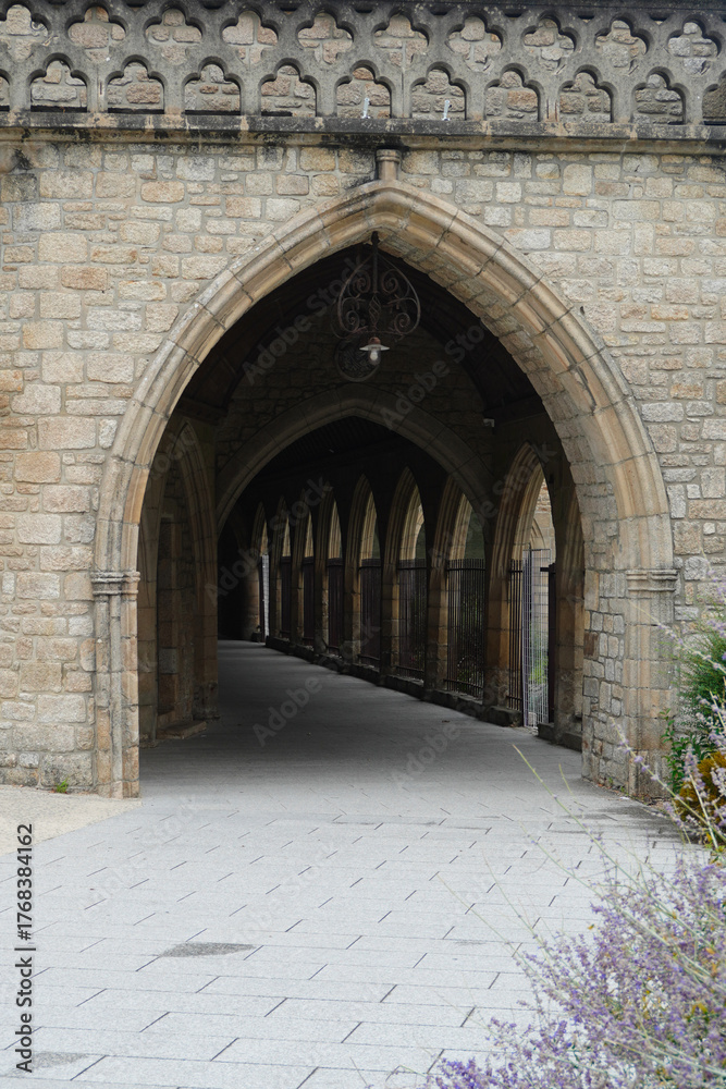 Naklejka premium Gothic stone arcade in Dinan, Brittany, France. Elegant pointed arches and intricate details showcase medieval architecture and historic charm in this peaceful architectural passage