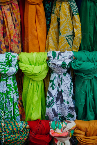 Colorful scarves displayed in a market stall, showing a variety of bright fabrics and patterns. The mix of textures and hues highlights craftsmanship and artistic textile design.