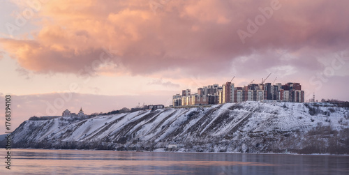 Panoramic view of new buildings in Krasnoyarsk. Orange sunset in winter on the banks of the ice-free Yenisei River in a city in Russia. New buildings and a newly built neighborhood with a beautiful