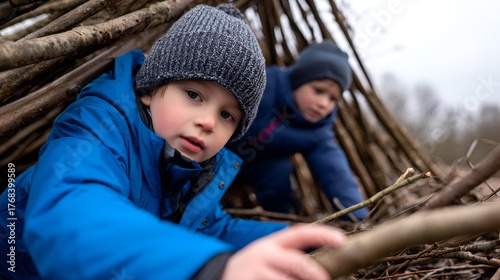 Two children playfully exploring a rustic stick fort in a serene outdoor setting on a cloudy day