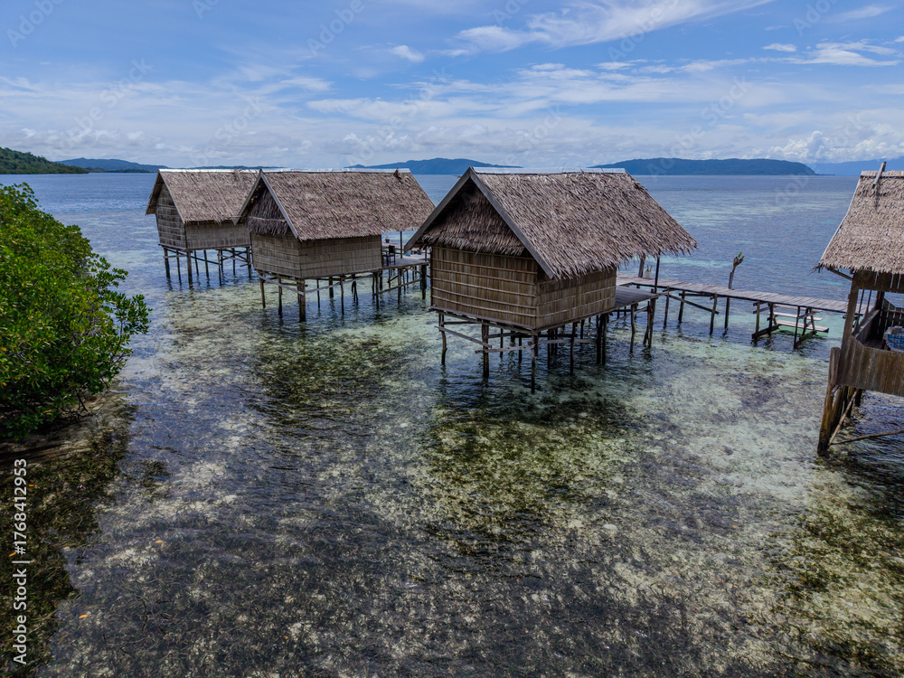 Fototapeta premium Traditional wooden stilt houses over shallow turquoise water in Raja Ampat, Indonesia, surrounded by coral and mangroves. 