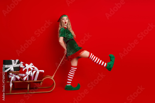 Fotografía Festive elf pulling sleigh with gifts in celebration of Christmas against a bold