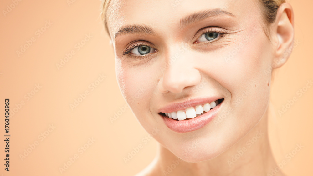 Obraz premium Beautiful young woman with clean fresh skin smiles radiantly against a soft peach background, showcasing natural beauty and confidence in a vibrant portrait
