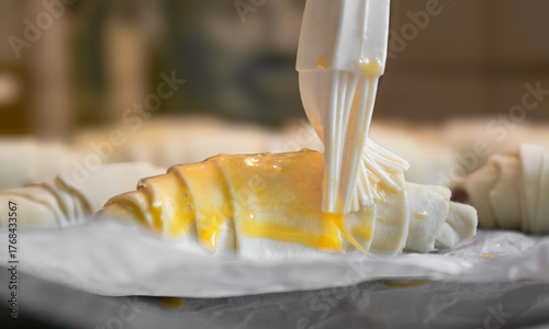 Baker brushing egg yolk on raw croissants on baking sheet