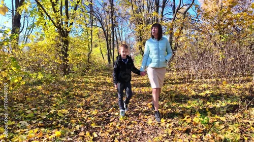 Mother and son walking on autumn leaves in sunny park