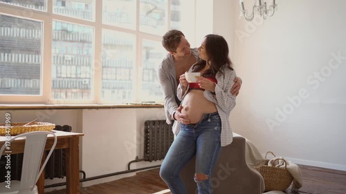 Pregnant wife and loving husband cuddling at home sharing smiles and baby dreams with tender embraces of her belly. man lovely kisses his wife. love and tenderness moments