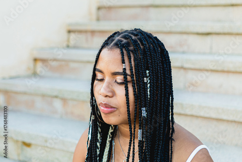 Portrait of a beautiful black woman with braids and eyes closed sitting on the street stairs