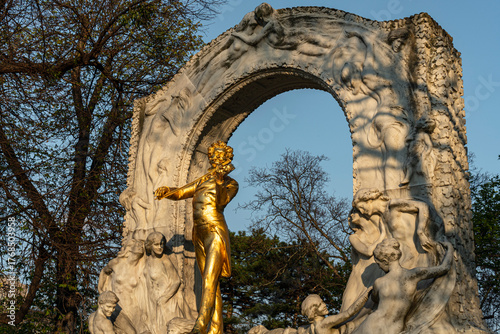 Golden Violinist Statue with Marble Arch and Sculptures in Sunlight