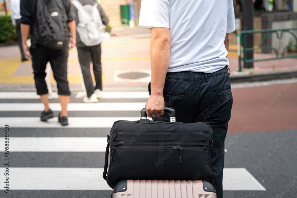 Fototapeta premium A working or traveler man is draging a luggage bag during crossing the road. Close-up from bag.