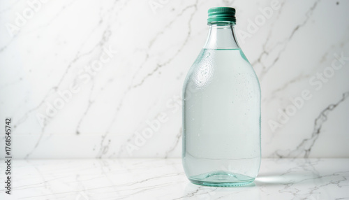 Minimalist flat lay photography of a glass bottle of alkaline water on a light marble background  