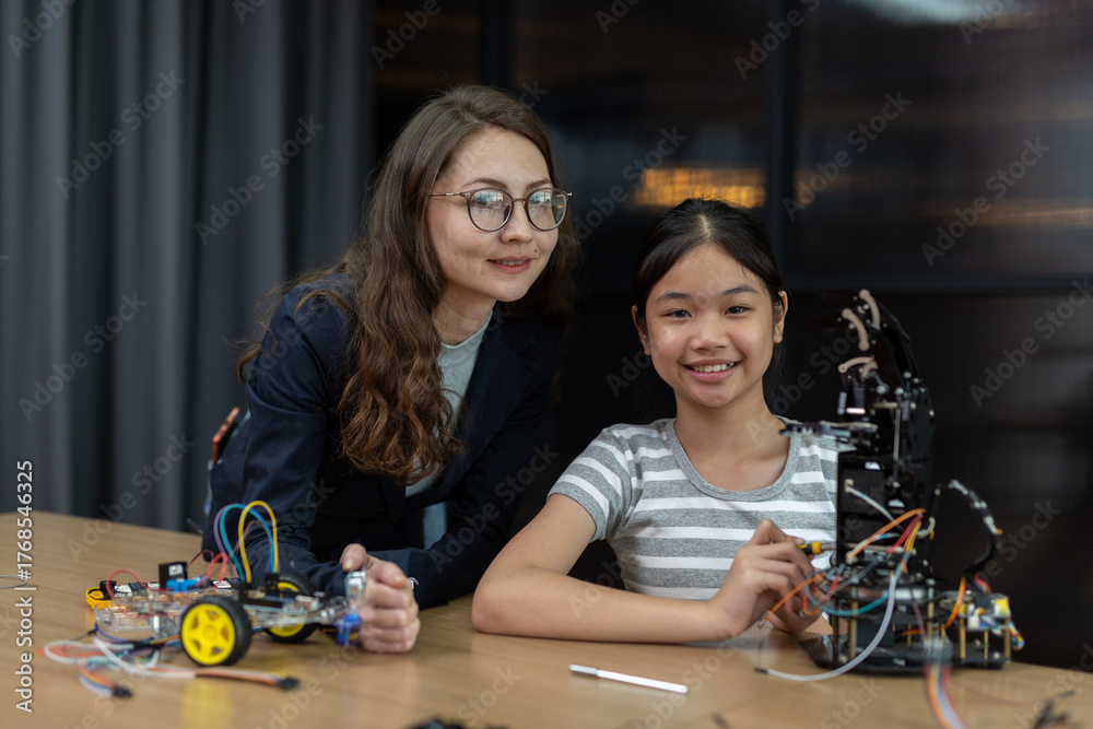 Fototapeta premium Female teacher mentoring girl in robotics project study in classroom, showcasing STEM education, innovation and learning with powered robotic arm. System skill training.