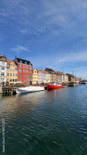 07 August, 2024, Copenhagen city center, Denmark Summer day scenic canal with boats and tourists, cyclists riding along colorful buildings and waterfront, vibrant urban atmosphere in European capital