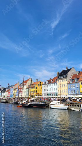 07 August, 2024, Copenhagen city center, Denmark Summer day scenic canal with boats and tourists, cyclists riding along colorful buildings and waterfront, vibrant urban atmosphere in European capital