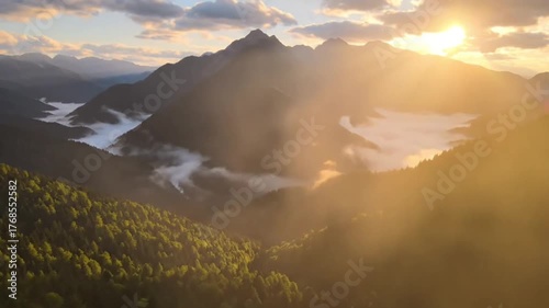 A breathtaking aerial drone shot of tall misty mountains covered in green forest, golden morning sunlight breaking through the clouds,