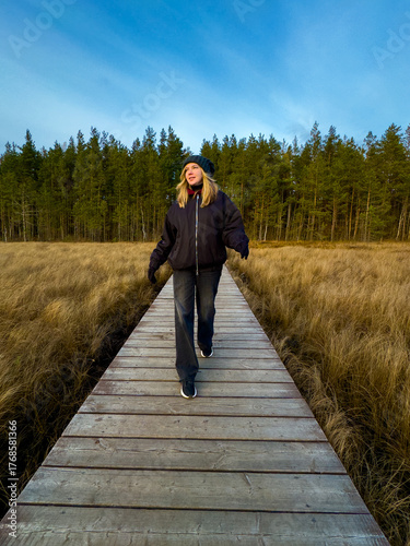 Joyful Young Woman Dancing on Boardwalk in Beautiful Autumn Nature