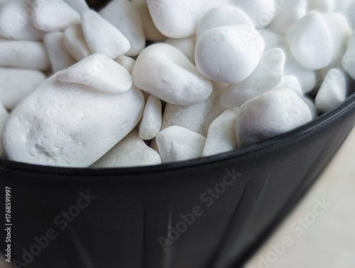 close-up of clean white smooth decorative pebbles or stones overflowing a black flower pot, texture background
