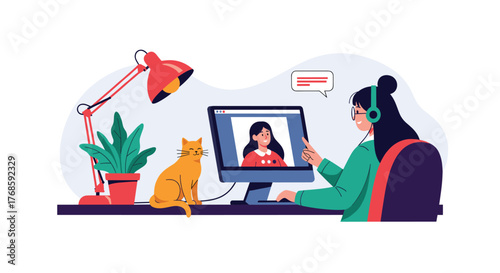 A person wearing headphones works on a computer with a cat nearby, a desk lamp and plant on the desk.