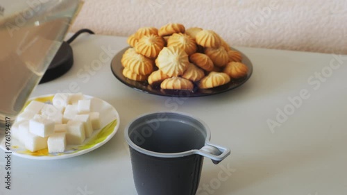 Hot water is poured from an electric kettle into a disposable mug of hot water. Medium shot.