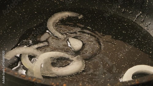 Onion rings being fried in a frying pan with vegetable oil. Medium shot.