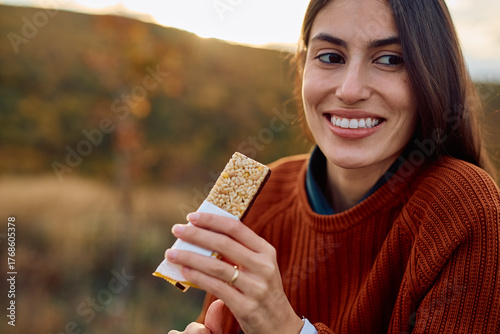 фотографія Smiling young woman eating a healthy snack bar, staying energized during an autu