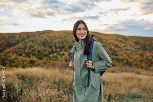 Young woman with backpack enjoying outdoors and fresh air, traveling in nature during fall season. Smiling at camera