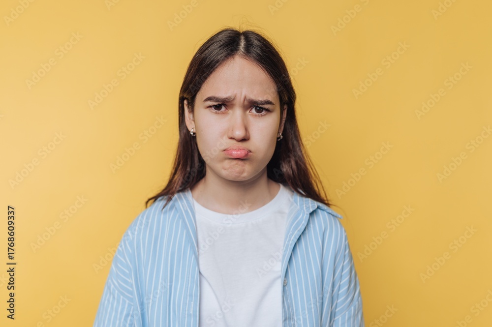 Obraz premium Young woman with a pouty expression against a yellow background.