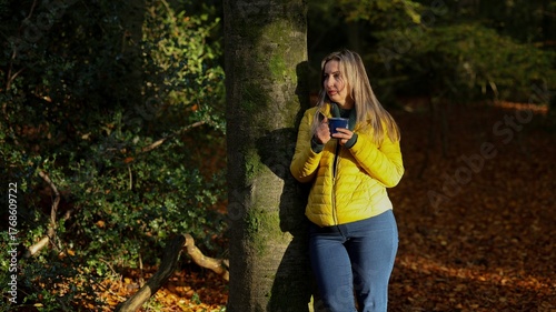 Woman Leaning Against a Tree Trunk, Enjoying a Hot Drink in the Autumn Forest