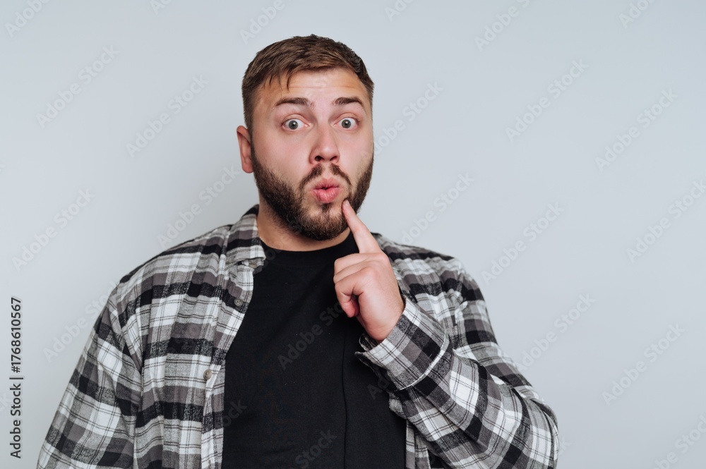 Obraz premium Man with surprised expression, wearing plaid shirt, finger on lips.