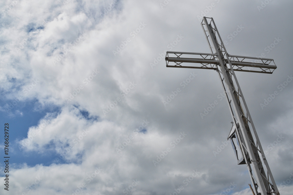 Fototapeta premium Steel lattice cross on top of a mountain against a blue sky and clouds