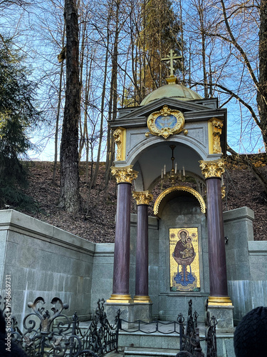 Ornate structure with golden dome and cross, surrounded by trees, showcasing intricate architectural details and religious symbolism in a serene outdoor setting
