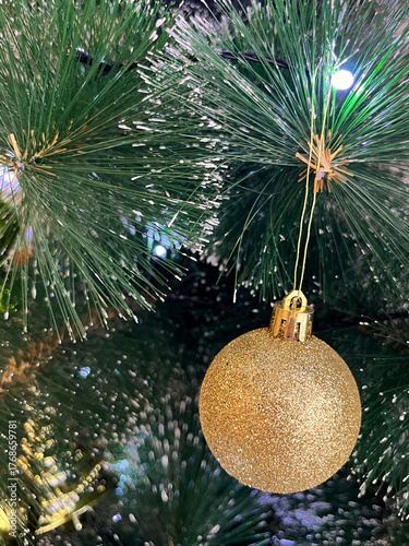 Golden glittering ornament hanging from a pine tree branch, surrounded by lush green needles, creating a festive atmosphere for holiday celebrations and seasonal decor