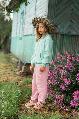 there are flowers near a wooden village house, and a child is standing next to them